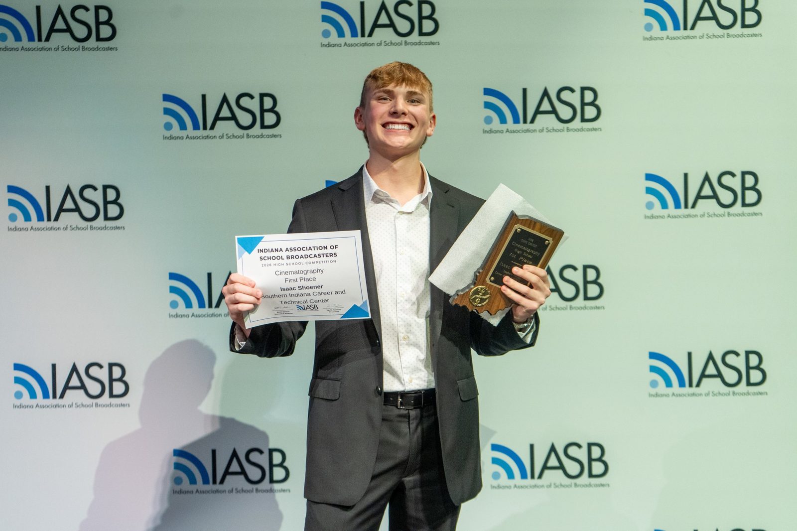 Isaac Shoener smiling and holding the first place certificate and plaque from the Indiana Association of School Broadcasters cinematography competition